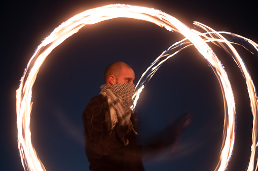 Man spinning fire poi at night in long exposure.