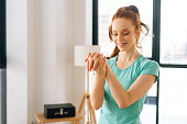 Medium shot portrait of smiling fit young woman doing stretching exercise wrist before fitness training at home office near window.