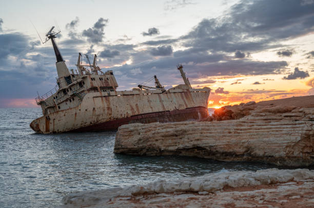 Abandoned rusty shipwreck resting on jagged coastal rocks at sunset, captured near the shoreline of Cyprus under dramatic skies.