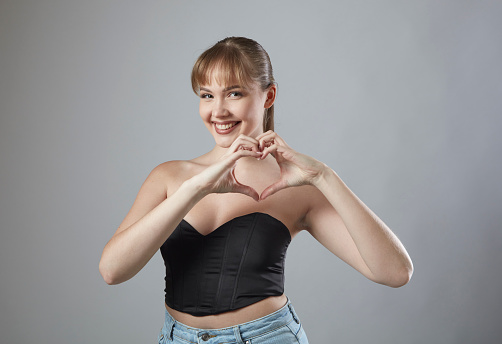 Smiling young woman with bangs making heart symbol with hands. Health is true happiness.