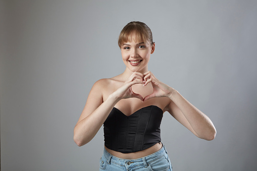 Smiling young woman with bangs making heart symbol with hands. Health is true happiness.