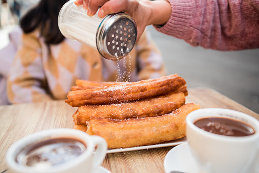 Woman's hand pouring sugar on the churros served on the bar table. in Valencia, Valencian Community, Spain