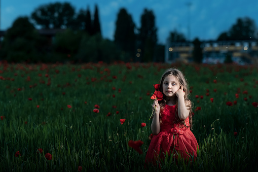 portrait of a little girl wearing a beautiful red dress ,she is lit artificially at the blue hour
