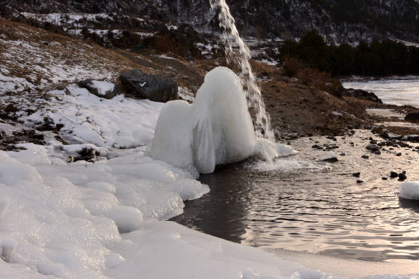A narrow stream of water flows down onto an ice block into a small backwater on a sunny winter day. Altai, Siberia, Russia.