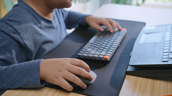 Close-up Hand of a child using a mouse and playing a game on a laptop at home, Asian boy 11 years old