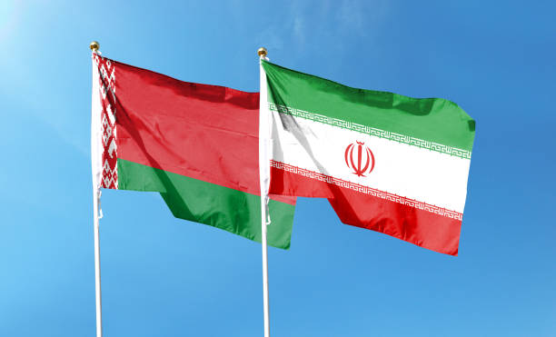 istock Iran flag and Belarus flag on cloudy sky. waving in the sky 1473606907