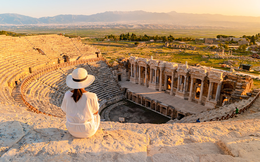 Hierapolis ancient city Pamukkale Turkey, a young woman with a hat watching the sunset by the ruins Unesco. Asian women watching sunset at the old Amphitheater in Turkey
