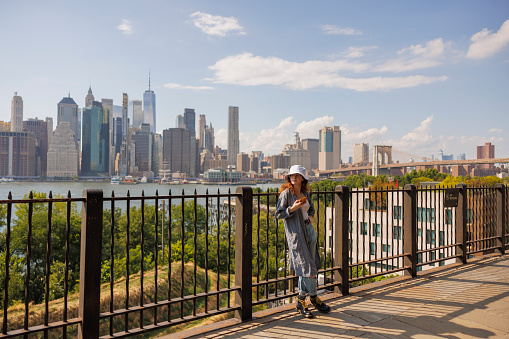 A young woman poses on the Brooklyn Heights Promenade overlooking Manhattan with famous One World Trade Center.