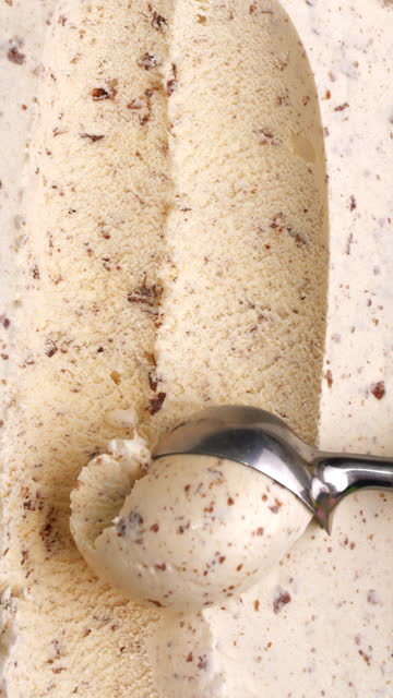 Chocolate chip-flavored ice cream is scooped into balls by an iron spoon.