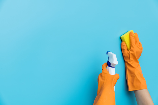 Woman hand cleaning blue wall with sponge.