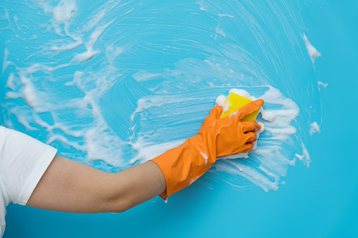 Woman hand cleaning blue wall with sponge.
