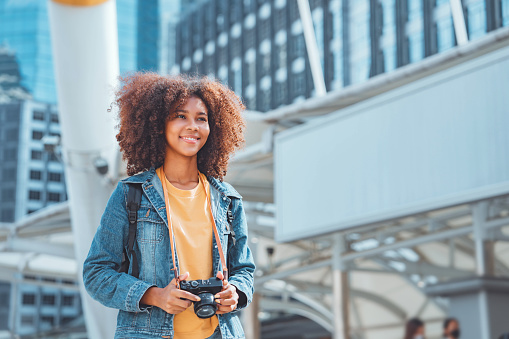 Happy young tourist African American woman holding a mirrorless camera on street in the city, Tourist journey trip concept