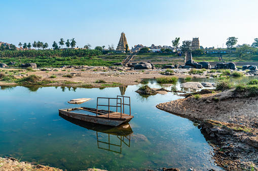 Wide shot of a  rusty sunk boat with Virupaksha Temple in the background