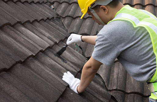 Worker man using waterproof roof coating repair to fix crack of the old tile roof.