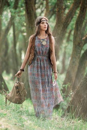 attractive young hippie woman walking among trees in forest . the concept of unity with nature