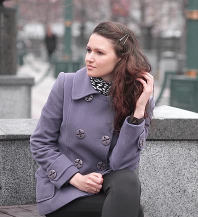 woman in fashionable coat sitting on bench in city.