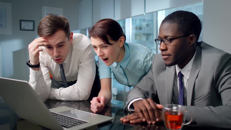 Portrait of shocked multiracial coworkers looking at laptop screen in modern boardroom