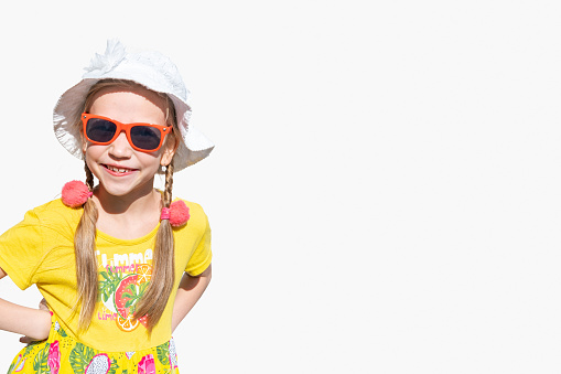 Children and summer. A happy emotional little girl in a hat, sunglasses and a yellow dress laughs and smiles at the camera on a white background, copy space.