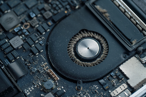 Close-up of a dirty laptop circuit board and a cooler fan with a lot of dust between the blades