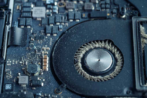 Close-up of a dirty laptop circuit board and a cooler fan with a lot of dust between the blades