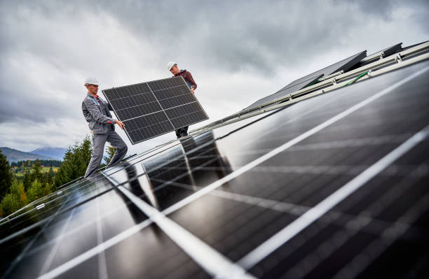 istock Technicians carrying photovoltaic solar module while installing solar panel system on roof of house 1473638840
