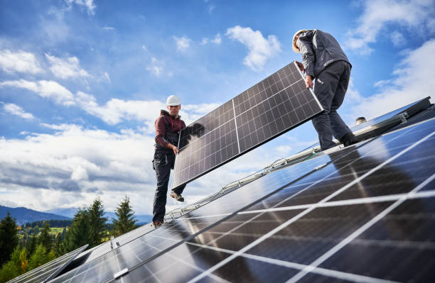 Technicians carrying photovoltaic solar module while installing solar panel system on roof of house stock photo