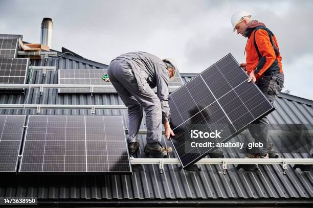 Technicians Carrying Photovoltaic Solar Module While Installing Solar Panel System On Roof Of House Stock Photo - Download Image Now