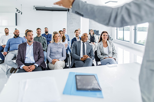 Happy business people listening to their colleague giving them a speech on education event in board room.