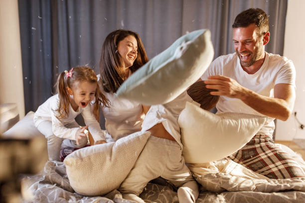 feliz familia teniendo una pelea de almohadas en el dormitorio. - bed couple pillow fight men fotografías e imágenes de stock