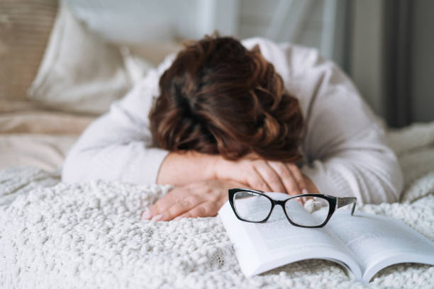 istock Sleeping middle aged woman withbook lying on bed at home 1473647769