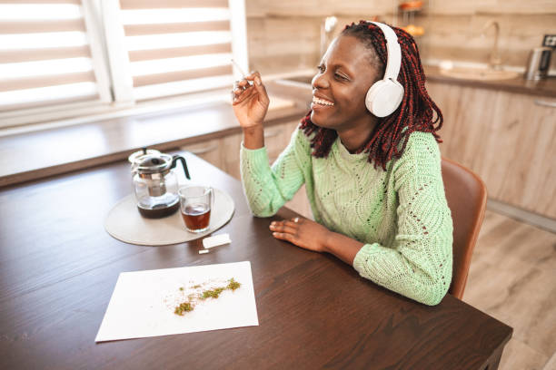 Smiling black adult woman making a cannabis joint Smiling black adult woman making a cannabis joint and listening to music smoking women luxury cigar stock pictures, royalty-free photos & images