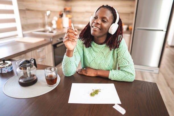 Smiling black adult woman making a cannabis joint Smiling black adult woman making a cannabis joint and listening to music smoking women luxury cigar stock pictures, royalty-free photos & images