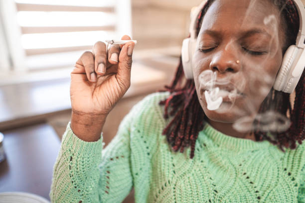 Portrait of a smiling adult black woman smoking a cannabis joint Portrait of a smiling adult black woman smoking a cannabis joint and listening to music smoking women luxury cigar stock pictures, royalty-free photos & images