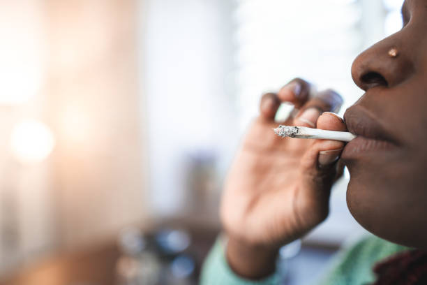 Portrait of a smiling adult black woman smoking a cannabis joint Portrait of a smiling adult black woman smoking a cannabis joint smoking women luxury cigar stock pictures, royalty-free photos & images