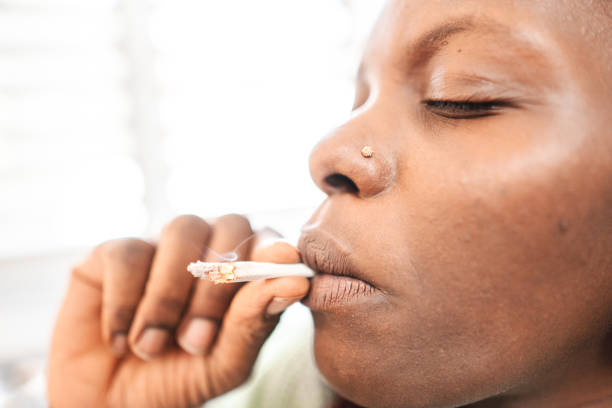 Portrait of a smiling adult black woman smoking a cannabis joint Portrait of a smiling adult black woman smoking a cannabis joint smoking women luxury cigar stock pictures, royalty-free photos & images