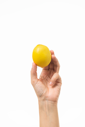 Unrecognizable female is holding one yellow lemon in hand in front of pure white background.