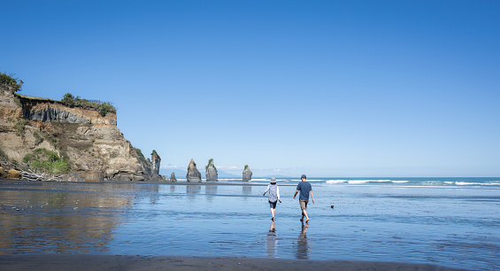 Couple walking towards Three Sisters, Mt Taranaki in the distance. Tongaporutu beach. Taranaki. New Zealand.
