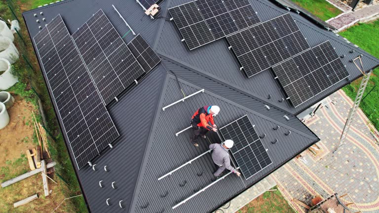 Technicians carrying photovoltaic solar module while installing solar panel system on roof of house