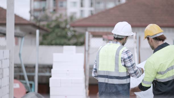 istock Professional civil engineer or building architect discussing with foreman about house model in blueprint in housing project construction site. Team of contractor in safety uniform working in real estate business. Concept of real estate business. 1473652713
