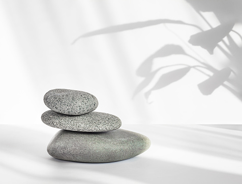 Close-up stack of stones on a gray background with a shadow of plants