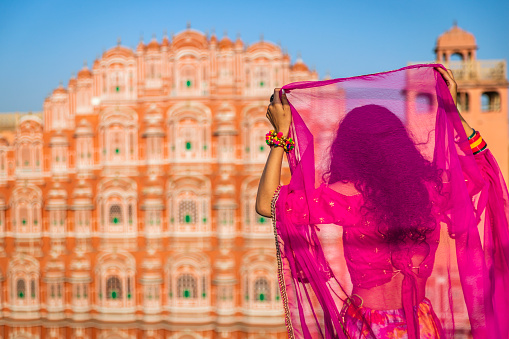 Young Indian woman, wearing sari, posing next to Hawa Mahal Palace, Jaipur, Rajasthan. The Hawa Mahal is the palace in the city of Jaipur - built from red and pink sandstone, it is on the edge of the City Palace.