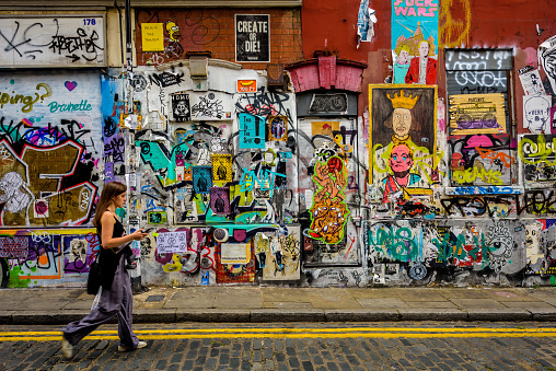 London, UK, July 15, 2017: A woman is seen walking against a graffiti-filled wall in the Shoreditch neighborhood