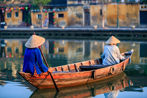 Vietnamese women in a row boat,, old town in Hoi An city, Vietnam. Hoi An is situated on the east coast of Vietnam. Its old town is a UNESCO World Heritage Site because of its historical buildings.