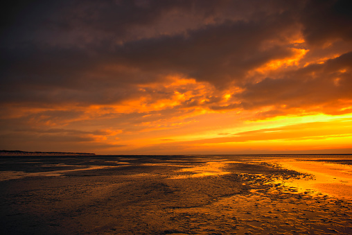 Colorful sunset at the North Sea beach of Schiermonnikoog island in the Dutch Waddensea region at the end of the day. Schiermonnikoog is part of the Frisian Wadden Islands and is known for its beautiful natural scenery, including sandy beaches, rolling dunes, and lush wetlands.