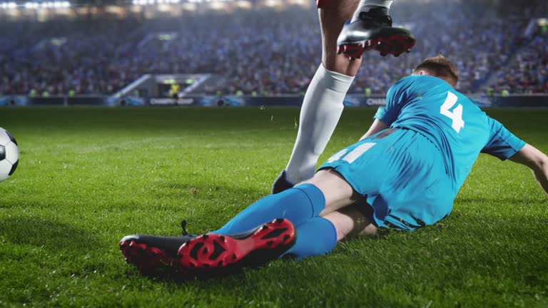 Aesthetic Shot of Blue Team Soccer Football Player Sliding on The Grass, Successfully Tackling the Opponent on Stadium With Croud Cheering. Super Slow Motion Captures Dangerous Sports Moment.