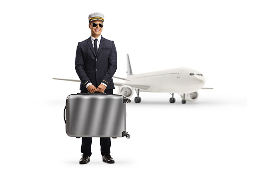 Pilot carrying a suitcase and and standing in front of an aircraft isolated on white background