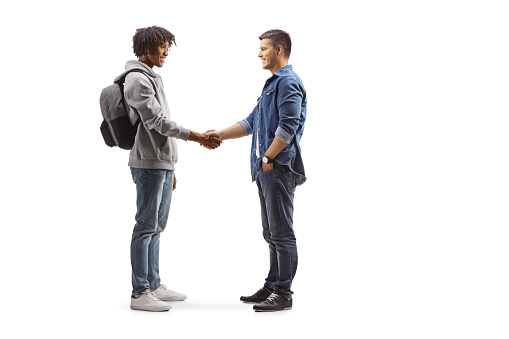 Full length profile shot of an african american male student and a caucasian man shaking hands isolated on white background
