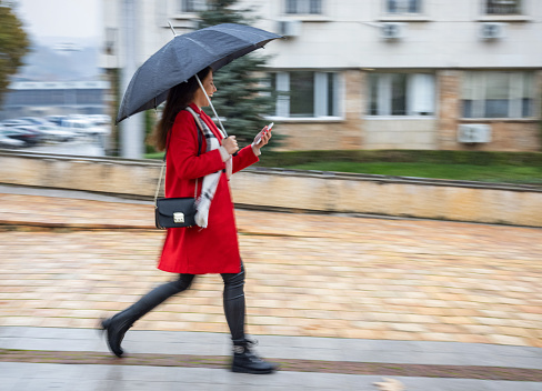 Motion blurred image of woman walking with black umbrella