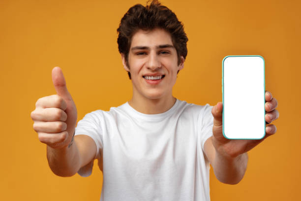 istock Smiling young man showing mobile phone blank white screen mockup to camera. 1473670921