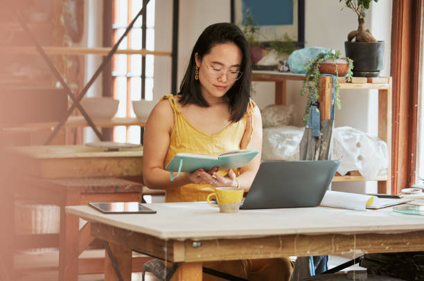 istock Startup, Asian or business woman reading book for research, knowledge or notebook for creative idea. Focus, thinking or girl with notes and laptop for planning social media, innovation or B2B review 1473671645